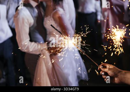 Sparkler in Händen auf einer Hochzeit - Braut, Bräutigam und Gäste, die helle Lichter halten Stockfoto
