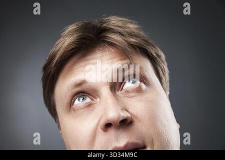 Nahaufnahme eines erwachsenen Mannes, der neugierig vor schwarzem Hintergrund aufblickt Stockfoto