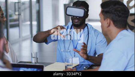 Erfahrender Arzt in blauen Peelings mit Stethoskop mit VR-Headset im Krankenhausbesprechungsbereich Stockfoto