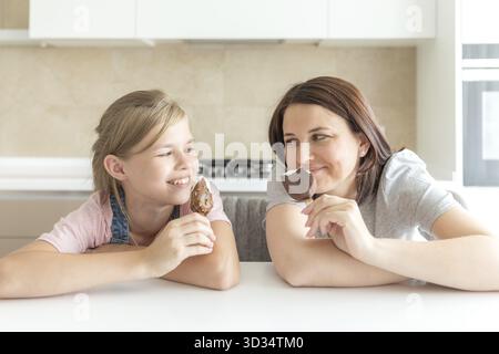 Mutter mit ihrer 12 Jahre alten Tochter in der Küche essen Eis sitzen. Gute Beziehungen von Elternteil und Kind. Glückliche Momente zusammen Stockfoto
