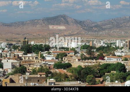Nikosia, Zypern Weitsicht auf Nikosia mit den Kyrenia-Bergen mit der riesigen Flagge Nordzyperns und einem türkischen Motto. Stockfoto