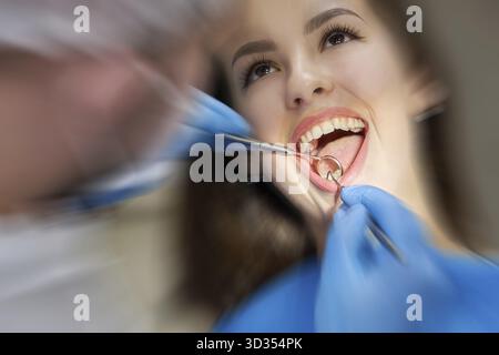 Nahaufnahme einer jungen Frau, die in der Zahnarztpraxis eine Zahnarztprüfung durchgeführt hat. Zahnarzt, der die Zähne eines Patienten mit zahnmedizinischen Werkzeugen untersucht Stockfoto