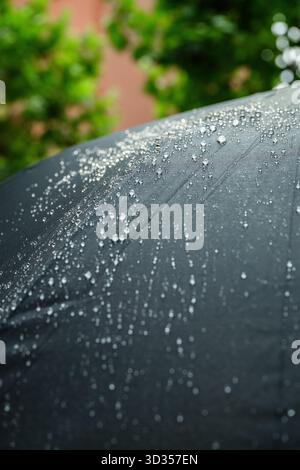 Nahaufnahme kleiner Wassertropfen auf einem dunklen Regenschirm nach Regen, mit wasserdichter Stoffstruktur und weichem natürlichem Außenlicht Stockfoto