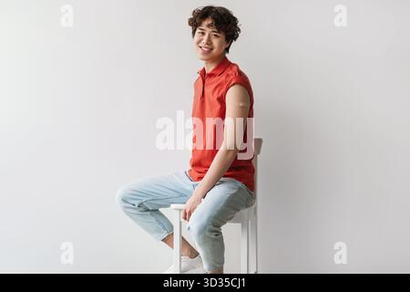Junger asiatischer Mann zeigt Arm mit Gips nach der COVID-19-Impfung im Studio Stockfoto