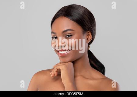Frau mit einem selbstbewussten Lächeln posiert anmutig vor einem neutralen Hintergrund während eines Beauty-Fotoshootings Stockfoto