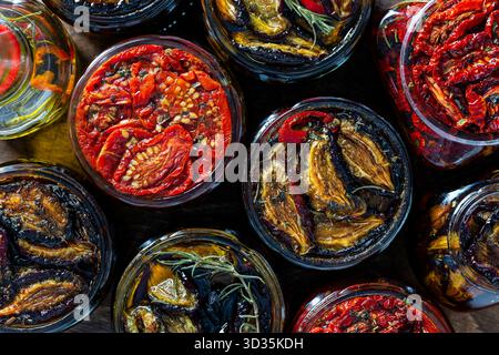 Sonnengetrocknete rote Tomaten und Pflaumen mit Knoblauch, grünem Rosmarin, rotem Chili, Olivenöl und Gewürzen in einem Glas auf einem Holztisch. Rustikaler Stil, Stockfoto