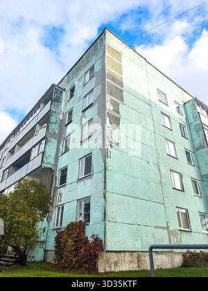 Altes Apartmentgebäude aus der Sowjetzeit mit gerissener Fassade und abblätternder Farbe unter blauem Himmel in Lettland Stockfoto