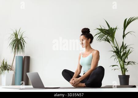 Yoga zu Hause mit einem Laptop genießt eine junge Frau ihre Meditationssitzung Stockfoto