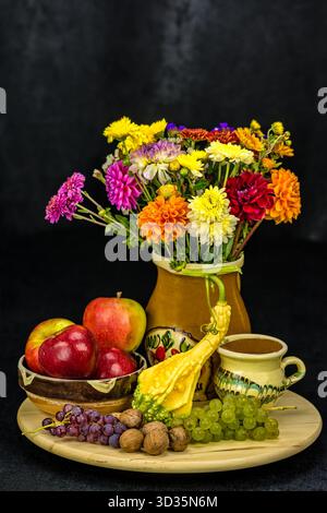 Farbenfrohes Bouquet mit Ringelblumen und Dahlien in einer Keramikvase, umgeben von Äpfeln, Trauben, Walnüssen und einem Kürbis. Ein reichhaltiges Stillleben mit Erntethemen Stockfoto