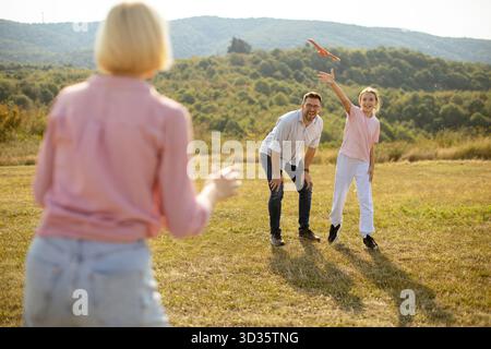Eine Gruppe von Freunden spielt Frisbee auf einem sonnigen Feld, umgeben von grünen Hügeln. Zwei Leute lächeln und lachen, während einer das Frisbee wirft. Stockfoto