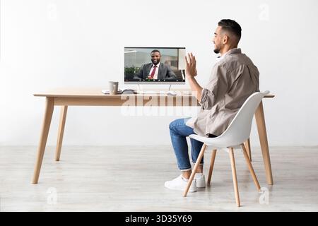 Ein junger arabischer Mann führt Videoanrufe mit einem Kollegen aus seinem Büro durch, lächelt und winkt Stockfoto
