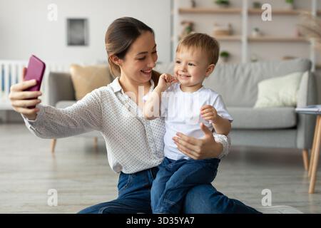 Mutter und Sohn haben gemeinsam Spaß bei einem Selfie zu Hause in einem warmen, einladenden Wohnzimmer Stockfoto
