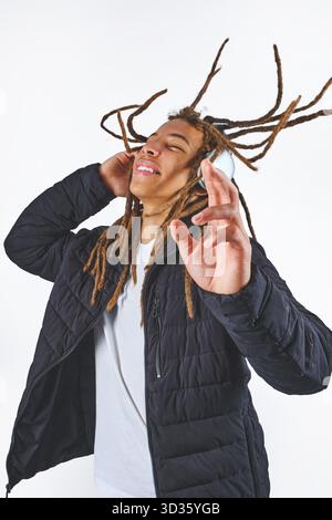 Junger Mann mit Dreadlocks und Kopfhörern, während er fröhlich Musik hört Stockfoto