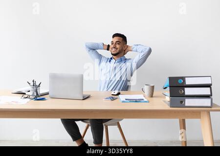 Ein lächelnder arabischer Mann macht eine Pause an seinem Arbeitsplatz und genießt einen Moment der Entspannung Stockfoto