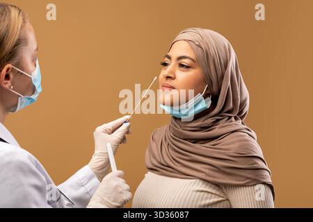 COVID-19 pcr-Testkonzept. Medizinisches Personal, das Nasenabstrich für Coronavirus-Probentest von infizierter muslimischer Frau nimmt Stockfoto