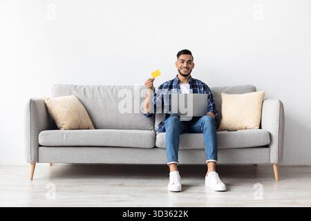 Fröhlicher Mann, der Online-Shopping von seiner gemütlichen Couch zu Hause genießt Stockfoto