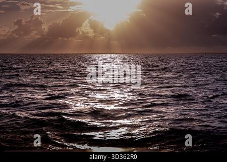 Untergehende Sonne bricht durch die Wolken über abgehacktem Wasser Stockfoto
