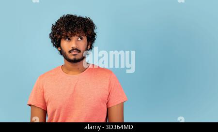 Neugieriger junger Mann, der nachdenklich in einem Studio vor blauem Hintergrund schaut Stockfoto