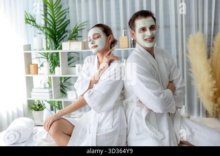 Glückliches Paar im Bademantel mit Gesichtscrememaske, das während des Urlaubs das ruhige Ambiente des Spa-Salons oder Hotels genießt. Verwöhnender Gesichtsbereich und Stockfoto
