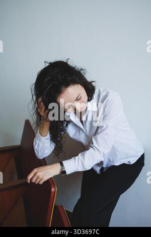 Eine junge Frau in einem formellen Hemd sieht nachdenklich aus, während sie sich sanft gegen eine Treppe beugt und einen Moment voller Introspektion elegant festnimmt Stockfoto