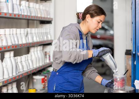 Mädchenkoloristin wählt die Farbe aus, indem sie verschiedene Farben für die anschließende Lackierung des Autos im Kfz-Service-Center mischt Stockfoto