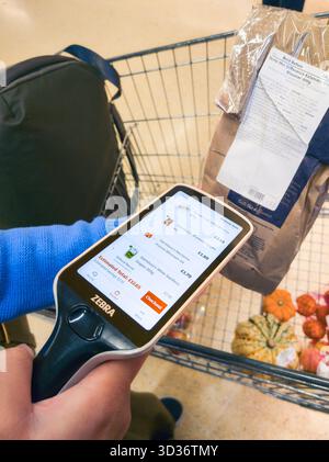 Frau, die einen Scanner zum Scannen von Produkt-Barcodes für Selbstkasse im Sainsbury Supermarkt verwendet, auch bekannt als Scan & Go, Smartshop & Self Checkout, Großbritannien Stockfoto