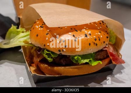 Saftiger Cheeseburger mit Sesambrötchen, geschmolzenem Käse, knusprigem Speck, frischem Salat und gegrilltem Rindfleisch auf einem Tisch im Restaurant. Konzept des Fast Food Stockfoto