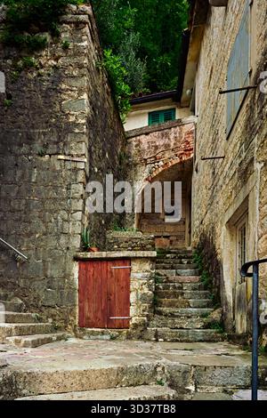 Alte Steintreppe, die unter einem Bogengang zwischen alten Mauern und einer Holztür in einer historischen Stadt führt Stockfoto