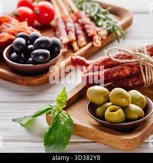 Ein rustikales Holzbrett bietet eine Auswahl an Vorspeisen, darunter Oliven, Kirschtomaten und Räucherfleisch, perfekt zum Teilen. Stockfoto