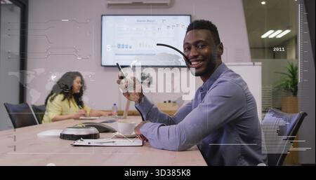 Telefon in der Hand, Geschäftsmann in blauem Hemd lächelnd am Besprechungstisch, mit Laptop, Becher, Kopierraum Stockfoto