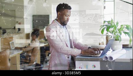 Schreibdesigner mit rosafarbenem Blazer am Stehtisch im Büro, mit Laptop, Rollplan und Pflanze Stockfoto
