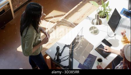 Kooperierende Softwareentwickler analysieren Code- und Datendiagramme im Büro, mit Laptops und Monitoren Stockfoto