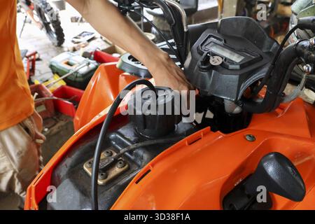 Fokussierter Mann, der in der Garage atv-Reparatur und -Wartung an einem orangen Fahrzeugmotor durchführt. Dieses leistungsfähige Quad-Bike ist ein erfahrener Mechaniker bei der Arbeit Stockfoto