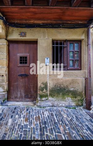 Nahaufnahme der rustikalen braunen Holztür und alten Steinfassade mit Fenster und Metallgrill in der historischen europäischen Stadt Stockfoto