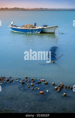 Kleines blaues und weißes Fischerboot vor Anker in der Lagune Etang de Canet, mit untergetauchten zylindrischen Netzen und schwimmenden Korken, Frankreich Stockfoto