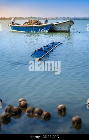 Blaues und weißes Fischerboot mit Netzen und Motor, verankert im stillen Wasser der Lagune, mit schwimmenden Korken im Vordergrund, Frankreich Stockfoto