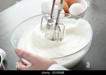 Frau, die Eiweiß mit Mixer am grauen Tisch schlägt, Nahaufnahme Stockfoto