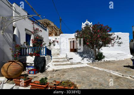 Amorgos, Griechenland - 11. September 2025: Straße mit Naturstein gepflastert, mit Stufen, die zu einer Kapelle und dem Burgfelsen im Hintergrund führen. Stockfoto