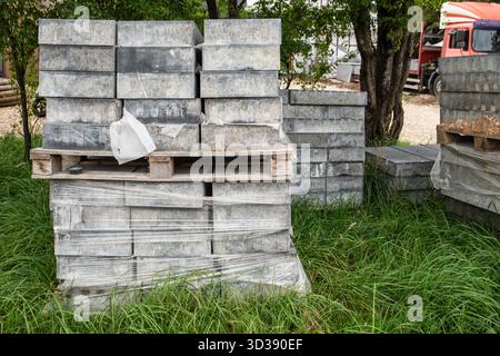 Stapel grauer Betonpflastersteine, ordentlich auf Paletten gestapelt und mit Kunststoff umwickelt, für den Einsatz in Bau- und Landschaftsbauprojekten vorbereitet. Stockfoto
