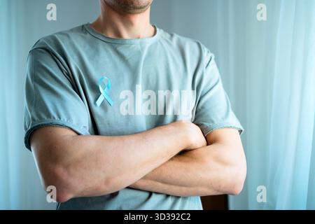 Mann, der mit überkreuzten Armen steht und blaues Satinband auf dem Hemd trägt. Konzept des Prostatakrebs Bewusstsein im November, Prävention, Früherkennung und medizinische Versorgung für die Gesundheit der Männer. Stockfoto