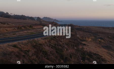Aus der Vogelperspektive auf eine gewundene Küstenstraße, die durch die goldenen Graslandschaften führt, während der pazifik den Horizont in der Nähe des Mendocino Headlands Stat küsst Stockfoto