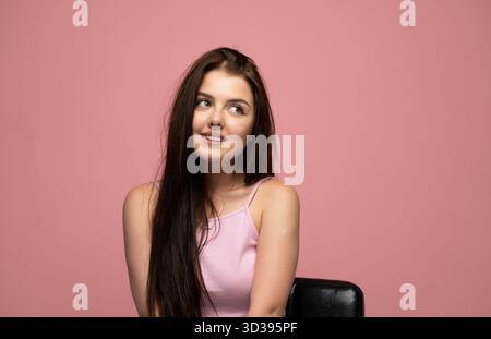Verspielte Emotion einer jungen Frau, die sanft in rosa Spitze auf rosa Hintergrund lächelt Stockfoto