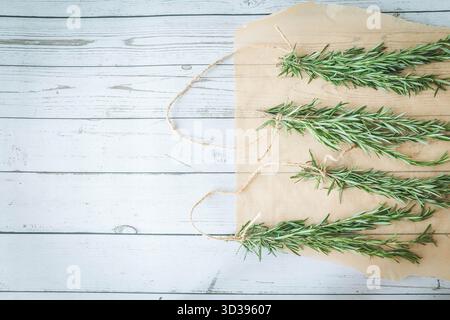 Vier Rosmarinbündel, zum Trocknen vorbereitet, gestylt auf Pergamentpapier mit hölzernem Hintergrund. Perfekt für saisonale Rezepte oder Kräuterhandwerk Stockfoto