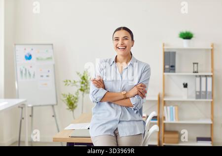 Schöne junge Frau, die die Arme überkreuzt hält, in die Kamera blickt und lächelt. Stockfoto