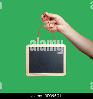 Die Hand eines Mannes hält ein kleines, leeres, leeres Tafel-Schild, das eine Mockup-Vorlage auf einem grün leuchtenden Hintergrund darstellt. Stockfoto