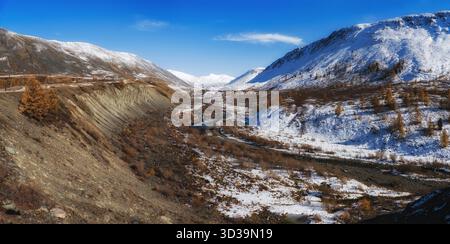 Panoramablick auf schneebedeckte Gipfel und herbstliche Bäume, mit einem Fluss im Hintergrund. Der erste Schnee der Saison in Altai. Schöner sonniger Tag. Stockfoto
