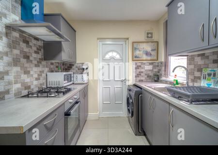 Moderne Küche mit grauen Schränken und Geräten, klarem Design und Tageslicht Stockfoto