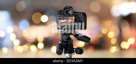 Professionelle Kamera vor verschwommenem Hintergrund mit Bokeh-Lichtern. Bannerdesign Stockfoto