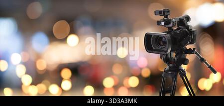 Videokamera auf Standfuß vor verschwommenem Hintergrund mit Bokeh-Lichtern. Bannerdesign Stockfoto
