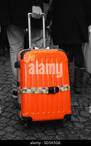 Touristen mit orangefarbenem Gepäck, die auf dem alten Pflasterpflaster spazieren gehen. Schwarzweißes selektives Farbfoto. Stockfoto